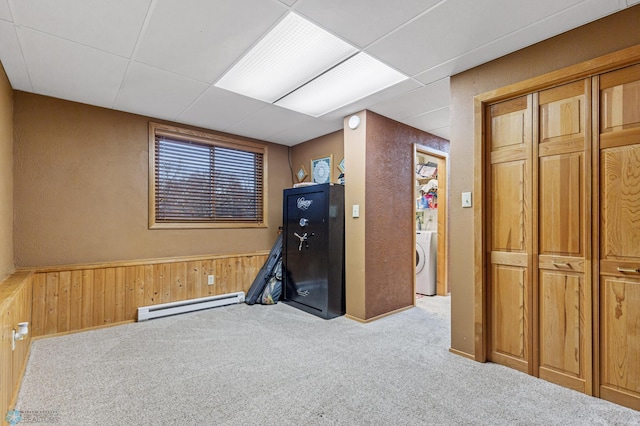 workout room with washer / dryer, a baseboard heating unit, a drop ceiling, light colored carpet, and wood walls