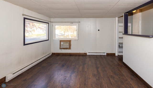 empty room with a wall mounted air conditioner, a drop ceiling, a baseboard radiator, and dark hardwood / wood-style flooring