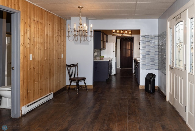 dining area featuring dark hardwood / wood-style flooring, a chandelier, a baseboard heating unit, and wood walls