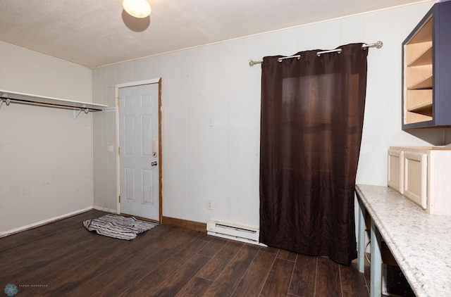 interior space featuring dark wood-type flooring, wood walls, a textured ceiling, and a baseboard heating unit