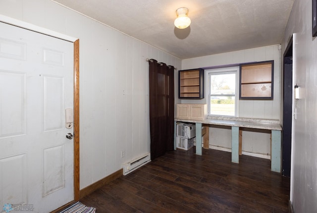 unfurnished office featuring a textured ceiling, wood walls, an AC wall unit, dark wood-type flooring, and baseboard heating