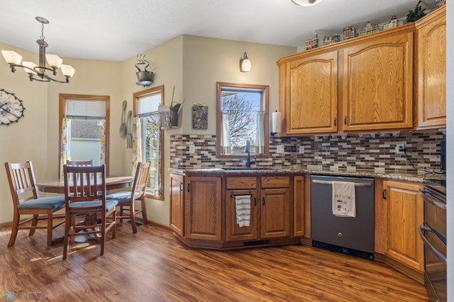 kitchen featuring hanging light fixtures, stainless steel dishwasher, dark hardwood / wood-style floors, dark stone countertops, and sink