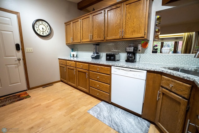 kitchen featuring tasteful backsplash, light stone countertops, white dishwasher, light hardwood / wood-style flooring, and sink