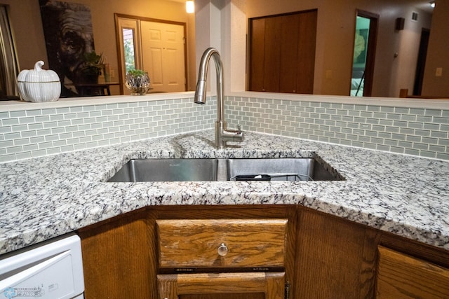 interior details with decorative backsplash, dishwasher, sink, and light stone countertops