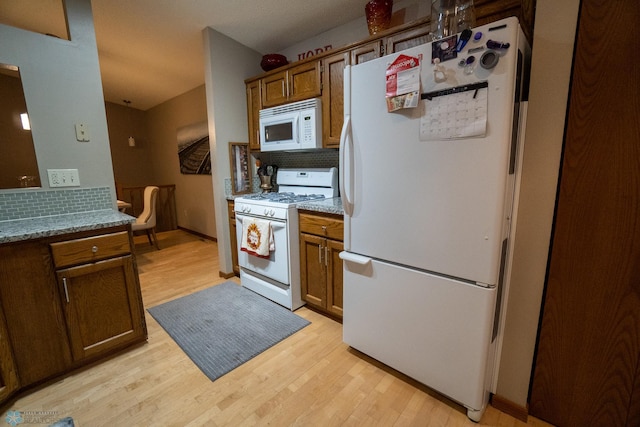 kitchen with decorative backsplash, light stone countertops, light wood-type flooring, and white appliances