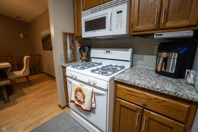 kitchen featuring decorative backsplash, light stone countertops, light wood-type flooring, and white appliances