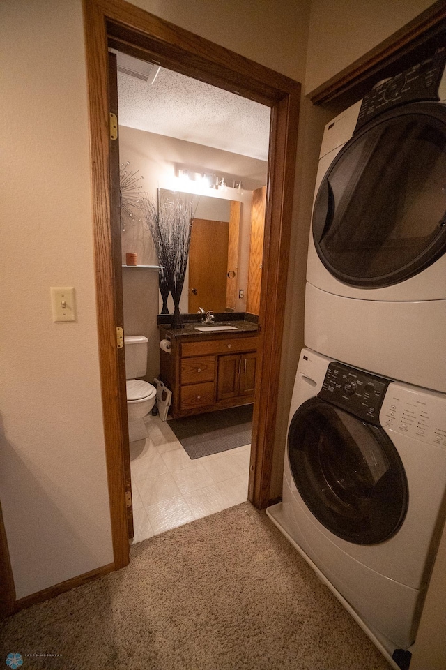 laundry area with stacked washing maching and dryer, a textured ceiling, sink, and light tile patterned floors