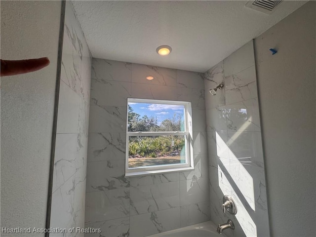 bathroom with tiled shower / bath combo and a textured ceiling