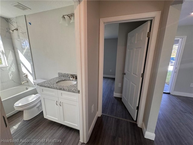 full bathroom featuring vanity, hardwood / wood-style floors, tiled shower / bath combo, and toilet