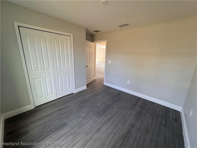 unfurnished bedroom featuring dark hardwood / wood-style floors, a textured ceiling, and a closet