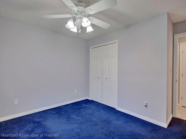 unfurnished bedroom featuring dark colored carpet, a closet, baseboards, and ceiling fan