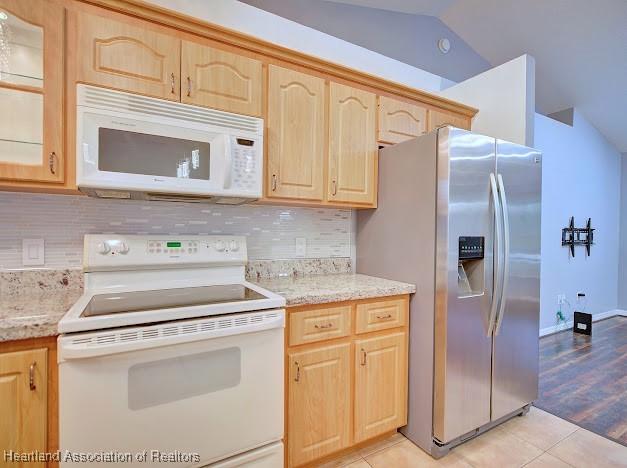 kitchen featuring light brown cabinets, decorative backsplash, white appliances, and vaulted ceiling