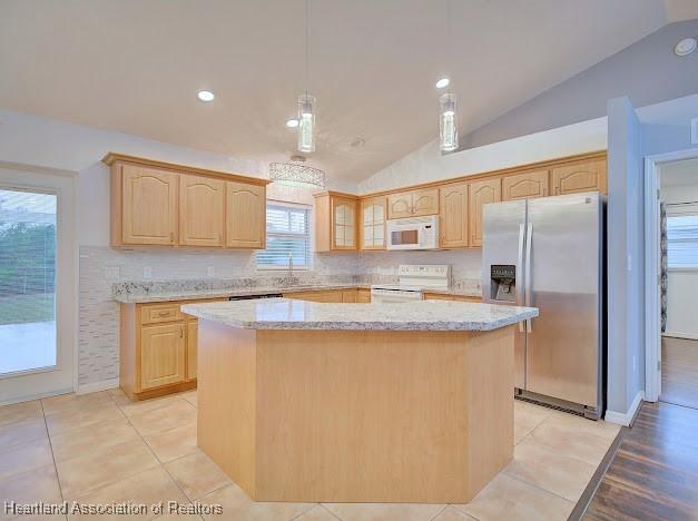 kitchen with light brown cabinets, light stone counters, a kitchen island, white appliances, and glass insert cabinets