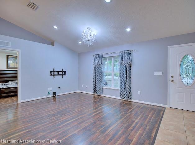 entrance foyer with wood finished floors, baseboards, visible vents, vaulted ceiling, and a chandelier