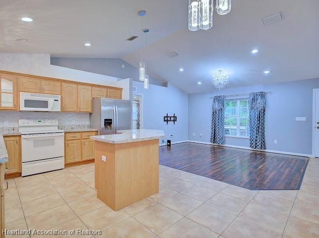 kitchen featuring light tile patterned flooring, white appliances, a kitchen island, and an inviting chandelier