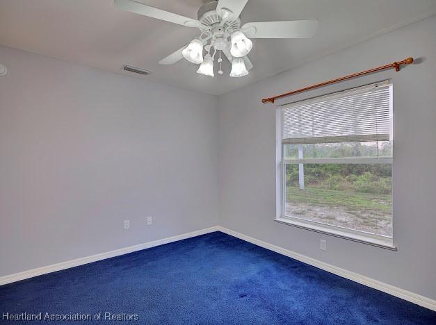 carpeted spare room featuring visible vents, a ceiling fan, and baseboards