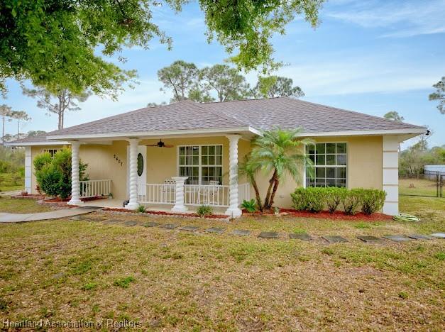 ranch-style house with a ceiling fan, roof with shingles, a porch, stucco siding, and a front lawn