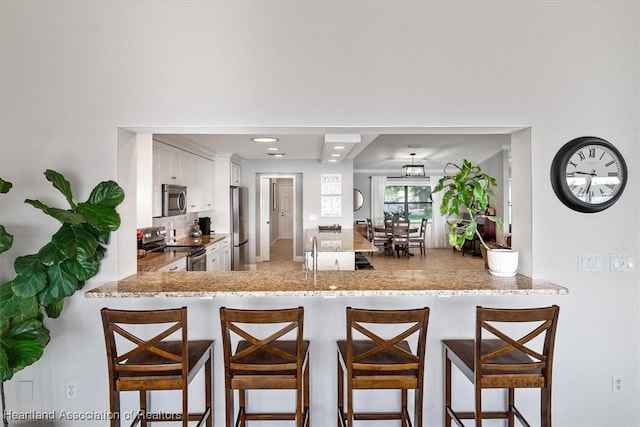 130 Deanna Dr, Lake Placid, FL 33852 - kitchen featuring appliances with stainless steel finishes, white cabinets, a peninsula, tasteful backsplash, and a breakfast bar