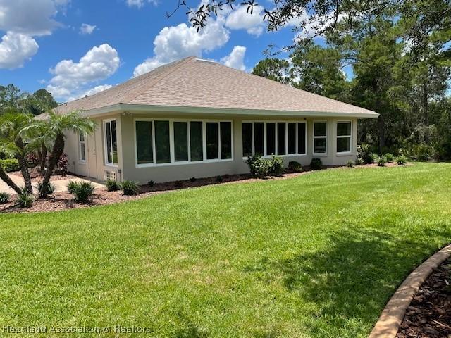 3929 Puma Dr, Avon Park, FL 33825 - rear view of house featuring a yard, stucco siding, and roof with shingles