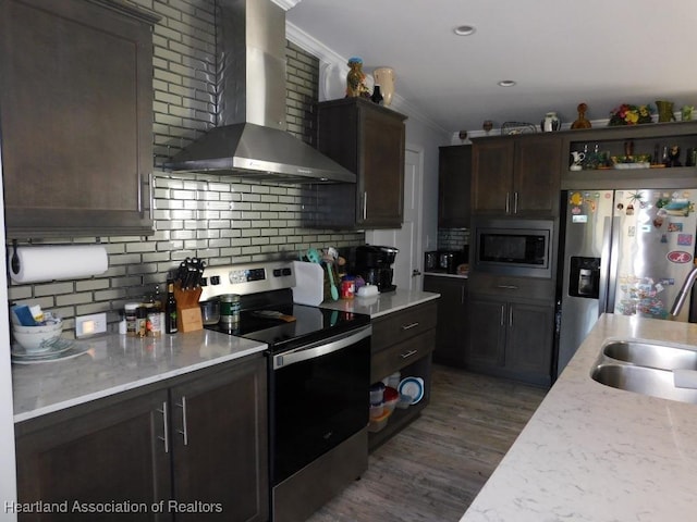 kitchen featuring wall chimney range hood, dark brown cabinets, ornamental molding, and appliances with stainless steel finishes