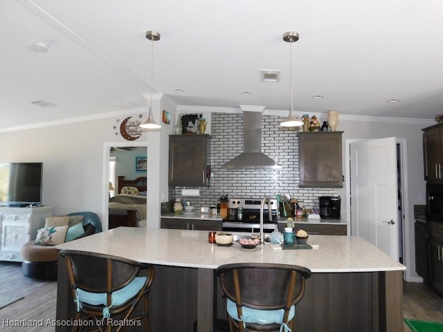 kitchen with wall chimney exhaust hood, stainless steel range with electric cooktop, light stone counters, dark brown cabinets, and a center island with sink