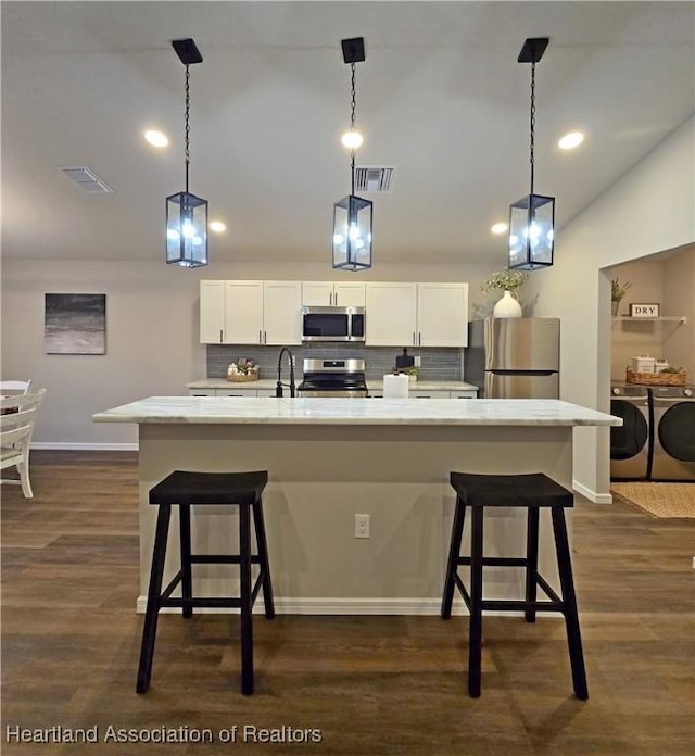 kitchen with decorative backsplash, appliances with stainless steel finishes, washer and clothes dryer, and a large island with sink