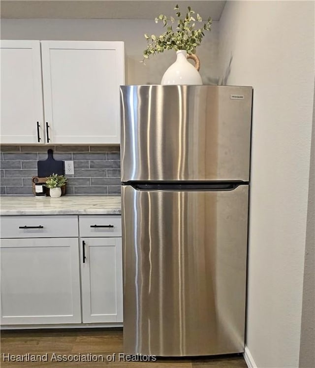 kitchen with decorative backsplash, stainless steel fridge, white cabinets, and light stone countertops