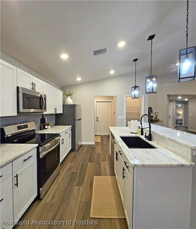 kitchen with backsplash, stainless steel appliances, a kitchen island with sink, sink, and white cabinetry