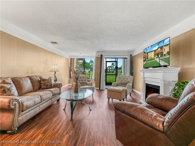 living room with a textured ceiling, a lit fireplace, dark wood-style flooring, and visible vents