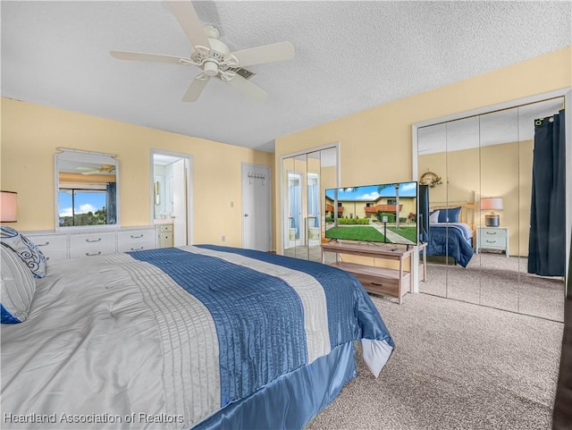 carpeted bedroom featuring a textured ceiling, ensuite bathroom, a ceiling fan, and multiple closets