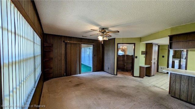 spare room with light carpet, a textured ceiling, ceiling fan, and wood walls