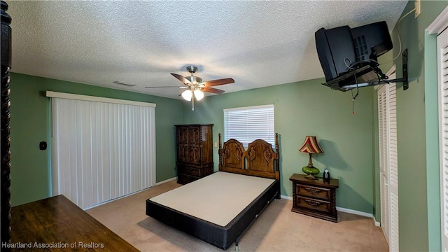 bedroom featuring ceiling fan, a closet, light carpet, and a textured ceiling