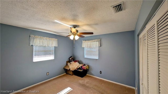 unfurnished bedroom with a closet, a textured ceiling, light colored carpet, and ceiling fan