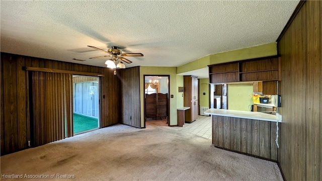 kitchen featuring ceiling fan, light carpet, kitchen peninsula, a textured ceiling, and wooden walls