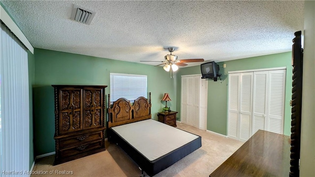 bedroom with ceiling fan, light colored carpet, a textured ceiling, and two closets