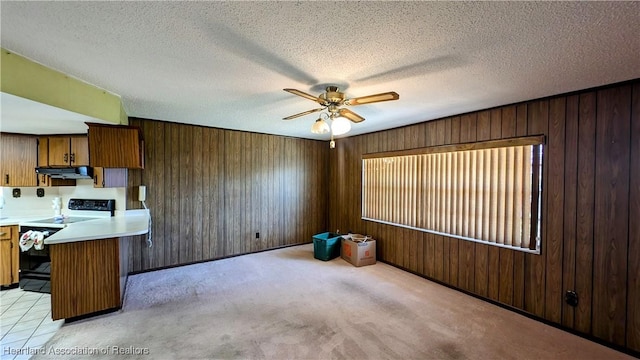 kitchen featuring wood walls, light carpet, black range with electric stovetop, a textured ceiling, and kitchen peninsula