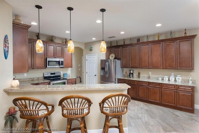 kitchen featuring a kitchen bar, decorative light fixtures, arched walkways, appliances with stainless steel finishes, and a peninsula