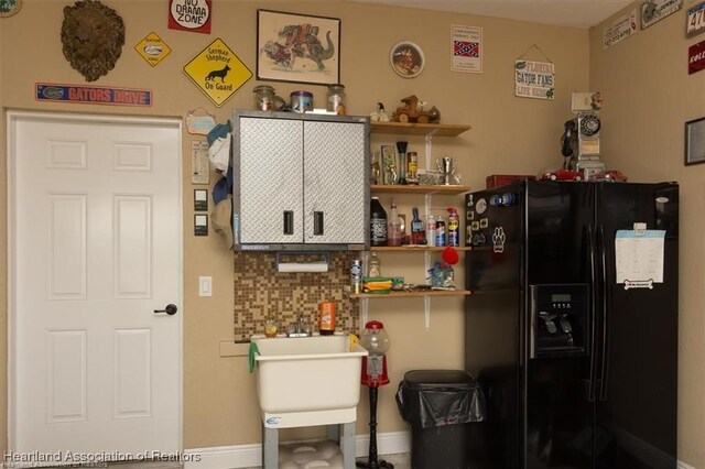 kitchen with open shelves, baseboards, and black refrigerator with ice dispenser