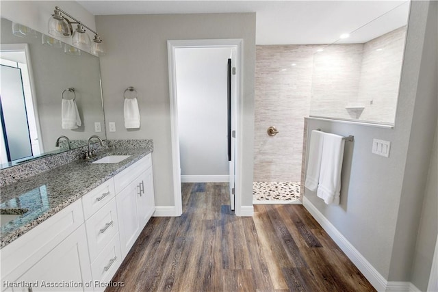 full bath with a walk in shower, wood finished floors, a sink, baseboards, and double vanity