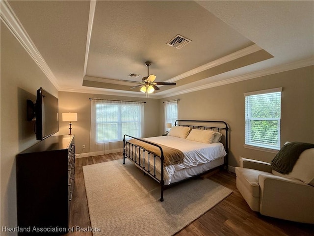 bedroom featuring dark wood-style flooring, visible vents, baseboards, a raised ceiling, and crown molding