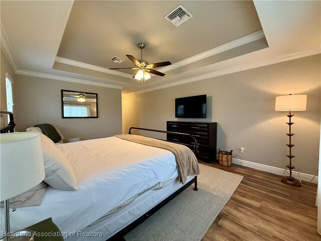 bedroom with a tray ceiling, visible vents, and wood finished floors