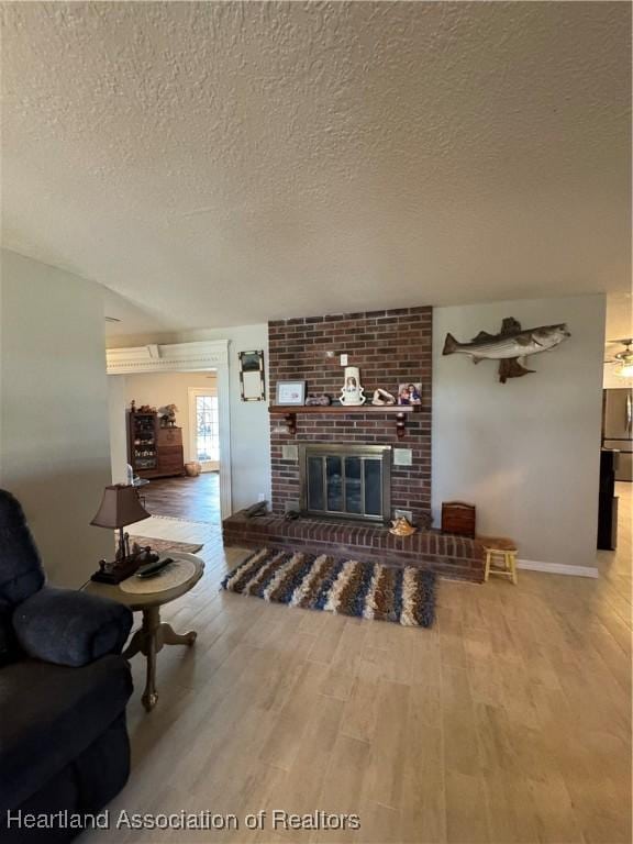 living area featuring a brick fireplace, a textured ceiling, and wood finished floors