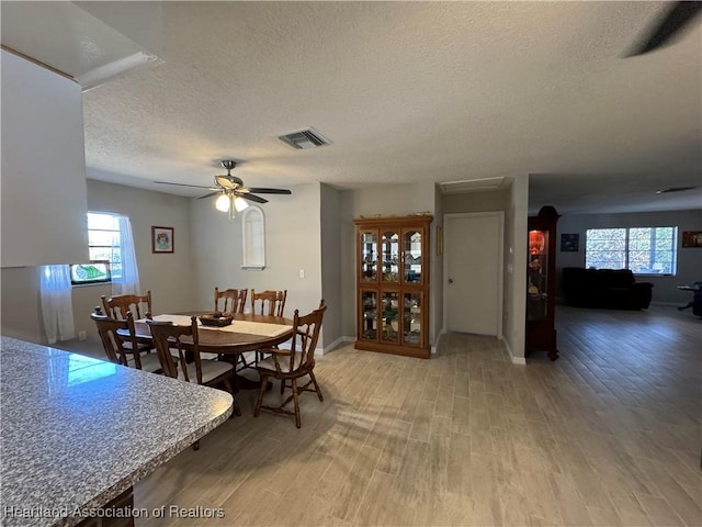 dining room with arched walkways, visible vents, light wood-style floors, ceiling fan, and a textured ceiling