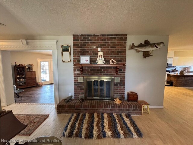 living area with a brick fireplace, a textured ceiling, and wood finished floors