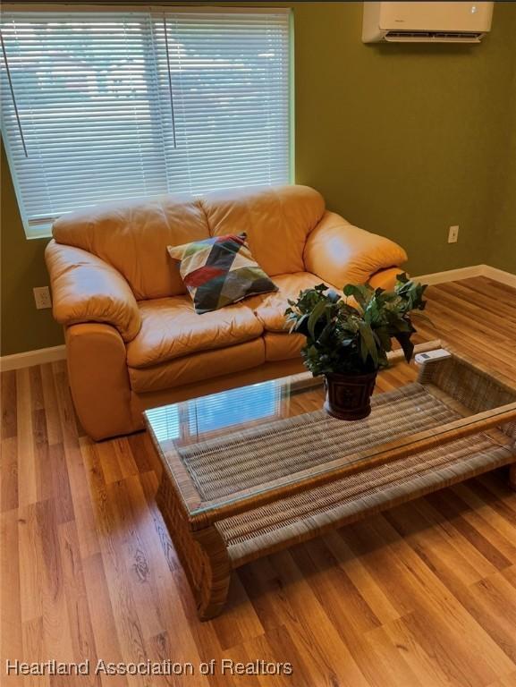 living room featuring a wall mounted AC, wood finished floors, and baseboards