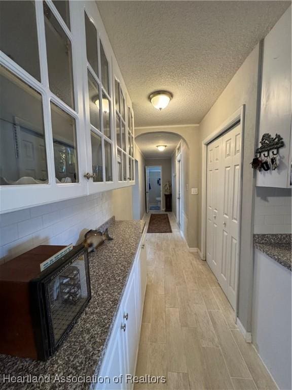 corridor featuring arched walkways, a textured ceiling, baseboards, and light wood-style floors