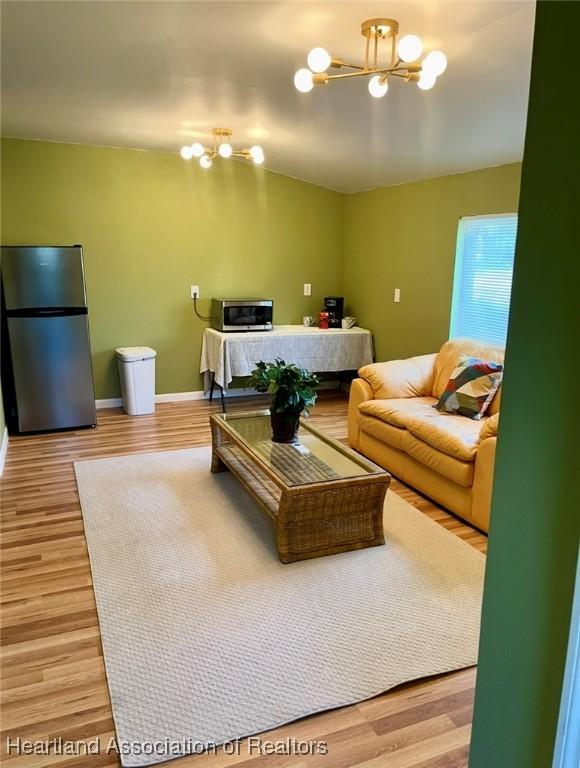 living room featuring vaulted ceiling, light wood-style floors, baseboards, and an inviting chandelier