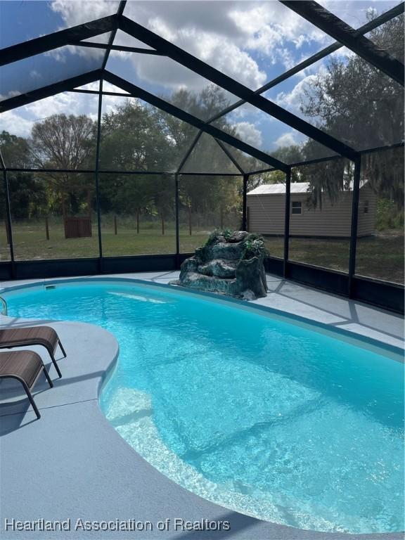 outdoor pool featuring an outbuilding, a yard, a patio, and glass enclosure