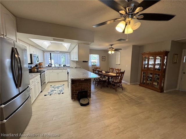 kitchen featuring a peninsula, a sink, baseboards, white cabinets, and appliances with stainless steel finishes