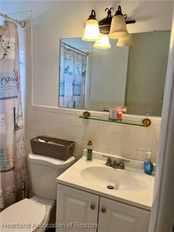 bathroom featuring toilet, curtained shower, vanity, and tile walls